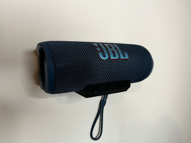 Peut inclure: Un haut-parleur Bluetooth portable JBL bleu fonc&eacute; avec une sangle noire. Le haut-parleur est recouvert d'un tissu textur&eacute; et le logo JBL est imprim&eacute; sur le c&ocirc;t&eacute;.