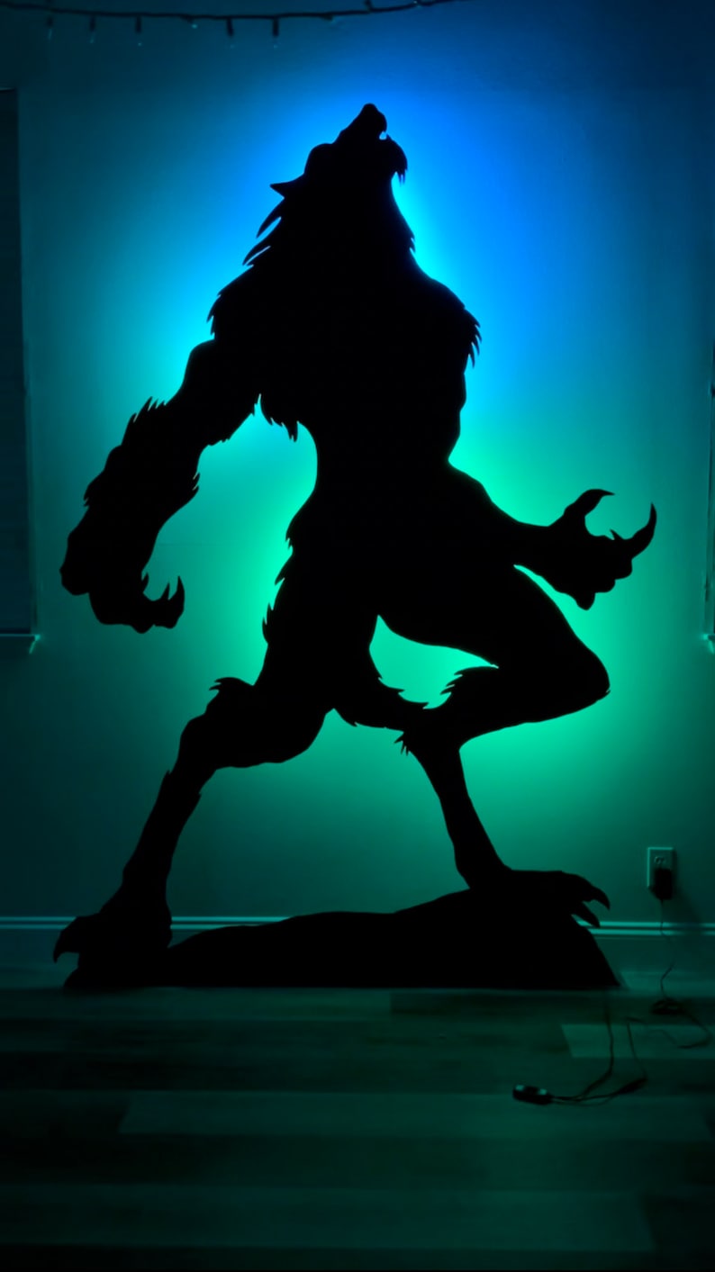 May include: A black silhouette of a werewolf howling at the moon, cut out of wood and illuminated with a blue and green light.