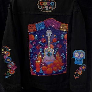 May include: Black denim jacket with colorful sequin and bead embellishments. Features a large back panel with a guitar, candles, and orange spheres. The word "COCO" is at the top, and a skull is on the right sleeve.