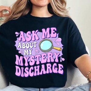 Puede incluir: Una camiseta negra con un gráfico morado que dice "Ask Me About My Mystery Discharge" con un gráfico de lupa.