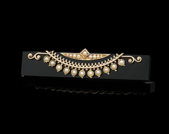 May include: A gold-toned bar pin with a decorative design featuring small pearls and a central diamond-shaped accent. The pin is set against a black rectangular base, creating a striking contrast. The design includes a series of dangling pearls.