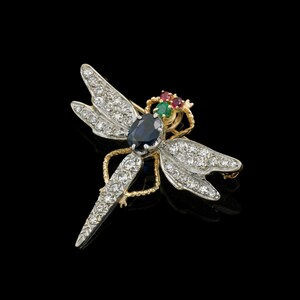 May include: A dragonfly brooch with a gold and silver-tone body. The wings are encrusted with small, clear gemstones. The dragonfly's body features a large, oval, dark blue gemstone. The head has a cluster of red and green gemstones.