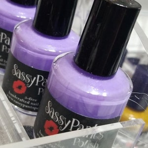 May include: Three bottles of purple nail polish with black lids and labels that say "Sassy Pants Polish" with a red lip print and the text "5-free handcrafted nail polish www.sassypantspolish.com"