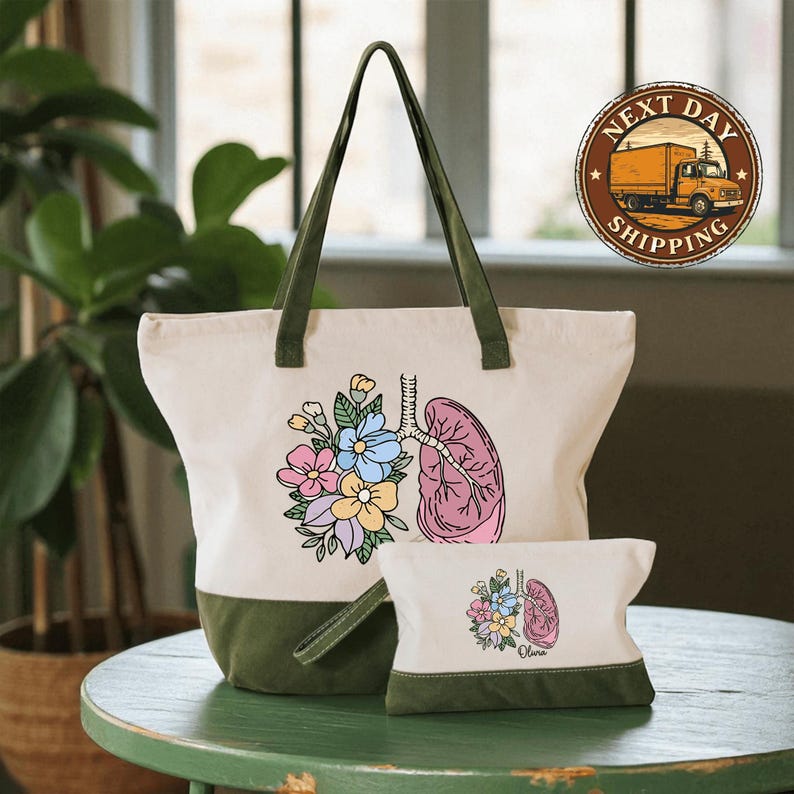 A white tote bag with a colorful floral design and a smaller bag with a similar floral design are displayed on a green table.