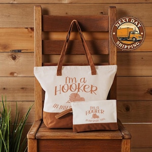 May include: A white canvas tote bag and matching pouch with brown accents. The tote bag and pouch have the text "I'm a Hooker in my spare time" printed in brown. The tote bag has brown handles.