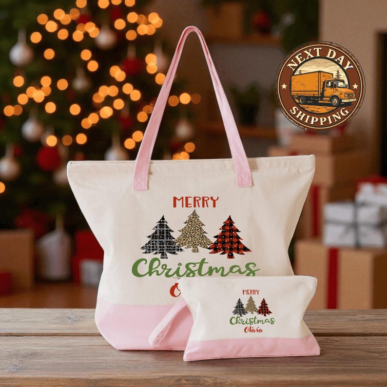 A white tote bag with a pink handle and a smaller bag with a Christmas tree design are displayed on a wooden surface, with a blurred background featuring a Christmas tree and other holiday decorations.