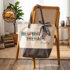 A tote bag with the text "RESPIRATORY THERAPY Emily" printed on it, sitting on a wooden chair in a room with a potted plant and bookshelves in the background.