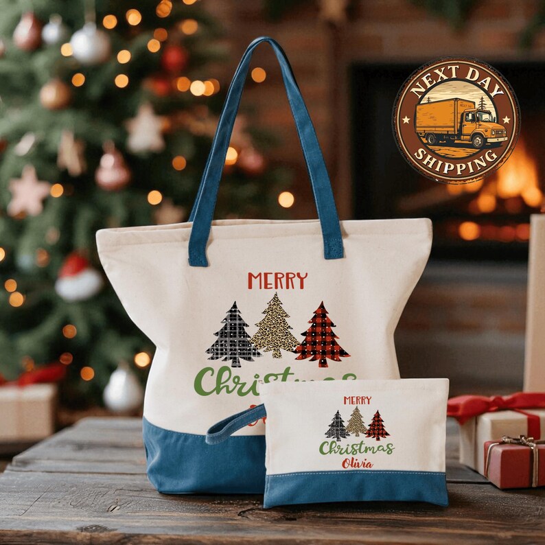 A white tote bag with a blue handle and a smaller white bag with a similar design are displayed on a wooden surface, with a Christmas tree and presents in the background.