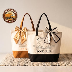 Two tote bags with bows and text, one white and one brown, are displayed on a woven mat.