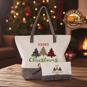 A white tote bag with a Christmas tree design and the text "Merry Christmas" printed on it, along with a smaller bag with a similar design, placed on a wooden surface in front of a lit fireplace.