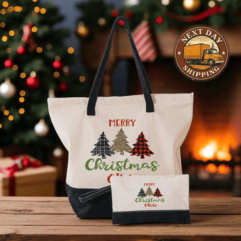 A white tote bag with a Christmas tree design and the text "Merry Christmas" printed on it, along with a smaller bag with the same design and text, placed on a wooden surface in front of a Christmas tree and a fireplace.