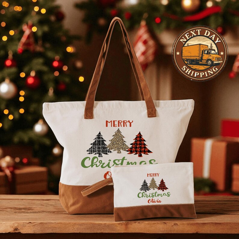 A white tote bag with a festive Christmas tree design and the text "Merry Christmas" printed on it, along with a smaller bag with the same design and text. The bag is placed on a wooden surface, and there is a Christmas tree and a truck in the background.