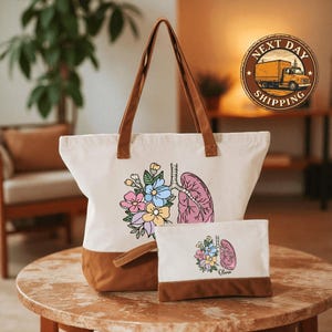 A white tote bag with a floral design and a smaller bag with a similar floral design are displayed on a wooden table.