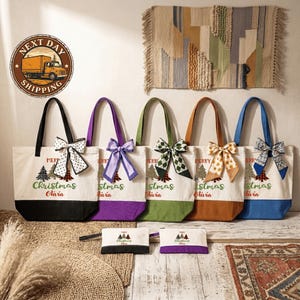 A collection of colorful tote bags with Christmas tree designs, each with a personalized name printed on them, displayed on a wooden floor against a wall with a rug.