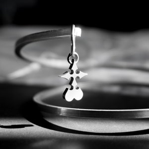 May include: A silver charm bracelet with a silver pendant shaped like a stylized cross. The pendant is hanging from the bracelet.