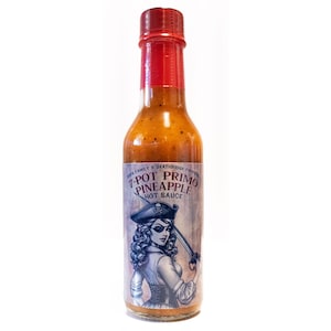 May include: A glass bottle of 7-Pot Primo Pineapple Hot Sauce with a red cap and a label featuring a pirate woman with a sword. The label is blue and white with the text "7-Pot Primo Pineapple Hot Sauce".