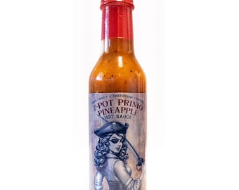 Könnte beinhalten: Eine Glasflasche mit 7-Pot Primo Pineapple Hot Sauce mit rotem Verschluss und einem Etikett, auf dem eine Piratenfrau mit einem Schwert abgebildet ist. Das Etikett ist blau und weiß mit dem Text "7-Pot Primo Pineapple Hot Sauce".
