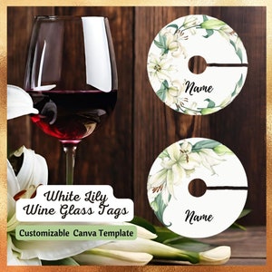 May include: Two white wine glass tags featuring a white lily floral design. The tags are round and have a cut-out for the stem of the glass. The text "Name" is printed on each tag. White Lily Wine Glass Tags Customizable Canva Template