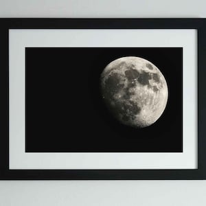 May include: A black and white photograph of a full moon in a black frame.