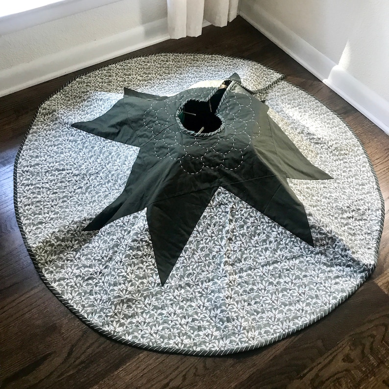 Peut inclure: Une jupe de sapin de No&euml;l matelass&eacute;e verte et blanche avec un motif d'&eacute;toile au centre. La jupe a un fond blanc avec un petit motif floral blanc et une &eacute;toile verte au centre.