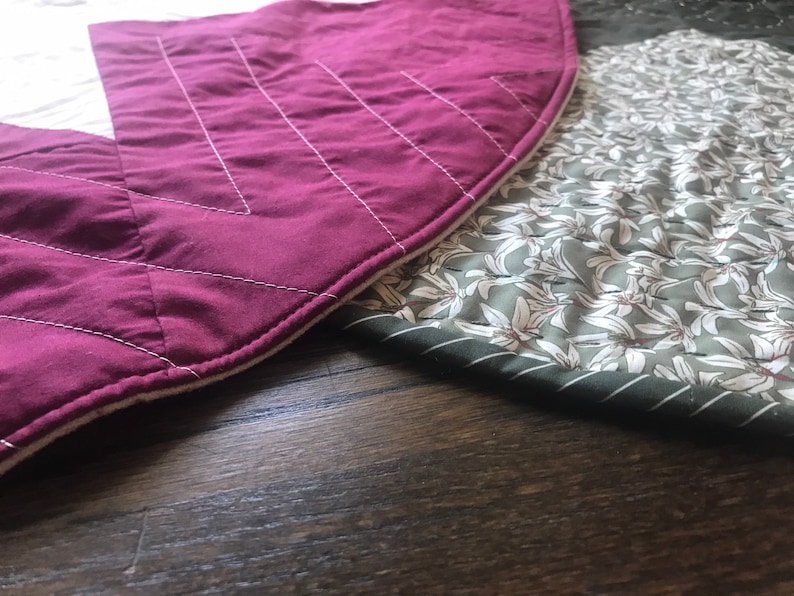 Peut inclure: Deux cercles de tissu matelass&eacute;s, l'un bordeaux avec des coutures blanches et l'autre vert avec un motif floral blanc. Les cercles de tissu sont pos&eacute;s sur une surface en bois fonc&eacute;.