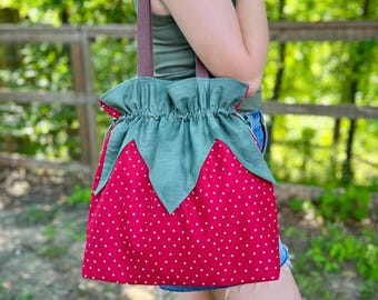 Peut inclure: Un sac fourre-tout rouge à pois blancs, conçu pour ressembler à une fraise. Le sac est doté d'un dessus vert en forme de feuille et de sangles marron. Le sac est en tissu et convient au transport d'articles.