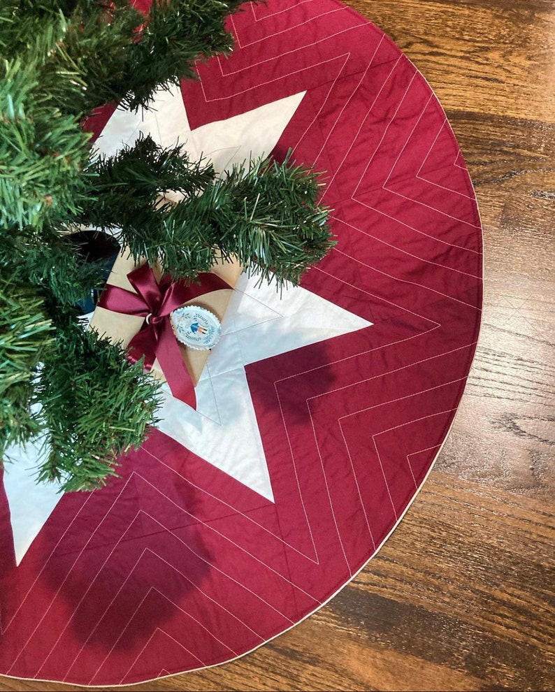Peut inclure: Une jupe de sapin de No&euml;l matelass&eacute;e rouge et blanche avec un motif en chevron. La jupe est d&eacute;cor&eacute;e d'une &eacute;toile blanche au centre.