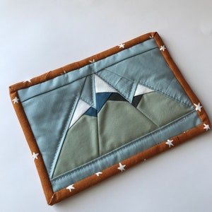 Peut inclure: Un design de montagne matelassé bleu et vert avec des étoiles blanches sur un fond brun.