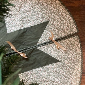 Peut inclure: Une jupe de sapin de No&euml;l matelass&eacute;e verte et blanche avec un motif d'&eacute;toile. La jupe a un motif floral blanc et une bordure verte avec une bande blanche.