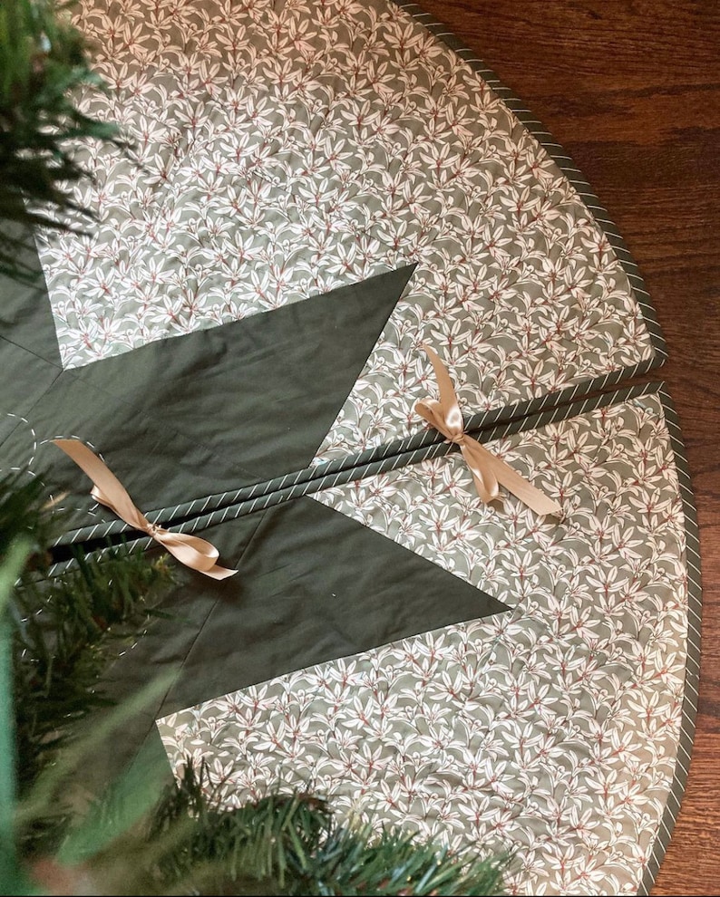 Peut inclure: Une jupe de sapin de No&euml;l matelass&eacute;e verte et blanche avec un motif d'&eacute;toile. La jupe a un motif floral blanc et une bordure verte avec une bande blanche.