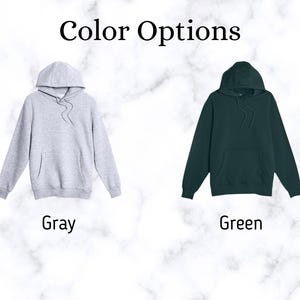 May include: Two hooded sweatshirts in gray and green are displayed against a marble background. The text "Color Options" is at the top. The gray hoodie is on the left, and the green hoodie is on the right. The word "Gray" is below the gray hoodie, and the word "Green" is below the green hoodie.