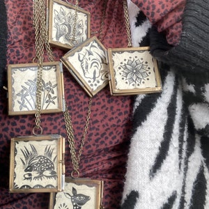 May include: A set of six brass framed pendants with black and white illustrations of animals and plants. The pendants are hanging on a chain and are worn as a necklace.