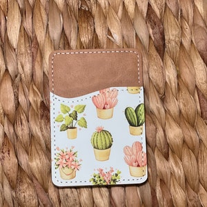 May include: A brown leather card holder with a white background and a pattern of pink and green cacti and plants.