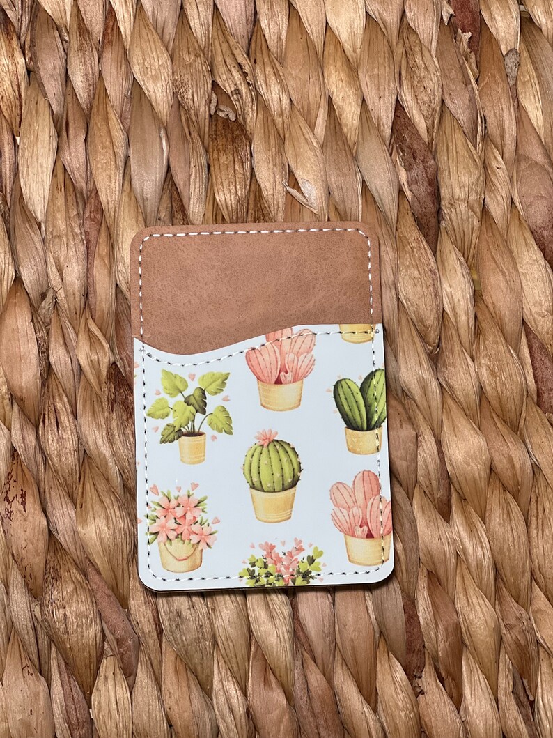 May include: A brown leather card holder with a white background and a pattern of pink and green cacti and plants.