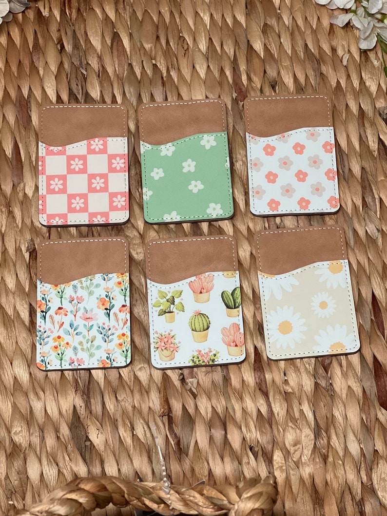 May include: Six different phone card holders with various floral and plant patterns. The card holders are brown with a suede-like texture and have a pocket for holding cards.