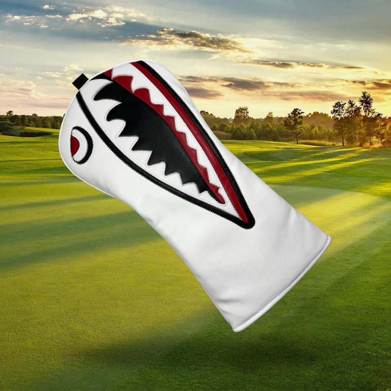 Op de afbeelding: Witte golfclubhoofdbeschermer met een haaienontwerp. De hoes heeft een witte basis met een rood en zwart haaienbekontwerp. De hoes is ontworpen om golfclubs te beschermen.