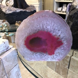 May include: A large, white agate geode with a pink, heart-shaped center. The geode is polished and has a smooth, shiny surface.