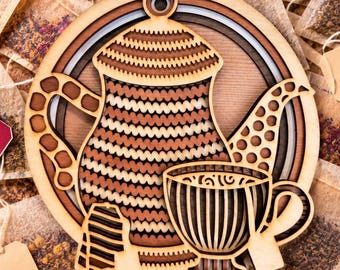 May include: A circular wooden wall hanging featuring a layered, laser-cut design of a teapot and a teacup. The teapot has a wavy, striped pattern in shades of light and dark brown, while the teacup displays vertical stripes and a handle.