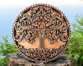 May include: A round, wooden wall art piece featuring a detailed tree of life design. The artwork is laser-cut with intricate patterns in shades of brown and black, and is displayed on a tree stump. The background shows a blurred lake and greenery.