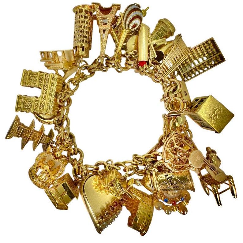 May include: A gold charm bracelet featuring various miniature charms, including the Eiffel Tower, a hot air balloon, and a heart. The bracelet is made of gold-toned metal and has a chain link design. The charms are detailed and represent different objects.