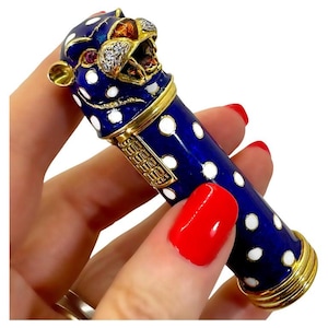 May include: A blue and gold lipstick case with white polka dots. The case features a detailed jaguar head with ruby eyes and diamond accents. The case has gold trim and a decorative gold clasp.