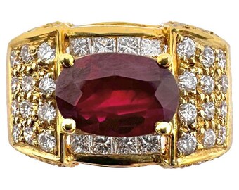May include: A gold ring featuring a large, oval-cut ruby as the centerpiece. The ruby is surrounded by smaller, round diamonds and square-cut diamonds, set in a gold band. The ring has a classic, luxurious design.
