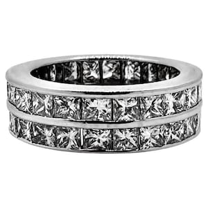 May include: A silver ring with two rows of square-cut, clear gemstones. The ring has a polished, reflective surface, and the gemstones are set closely together, creating a continuous band of sparkle. The ring is a piece of jewelry.