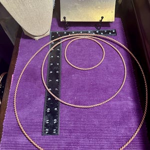 May include: Three copper-colored metal hoops of varying sizes are displayed on a purple surface. A ruler is placed next to the hoops for scale. A sign with the text "Goddess Factor" is in the background.
