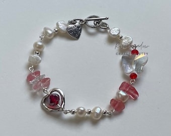 May include: A silver bracelet with a heart charm, white pearls, pink and red glass beads, and a butterfly charm. The bracelet has a toggle clasp.
