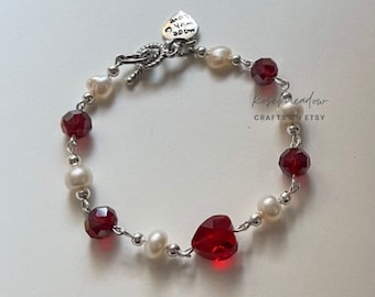 Op de afbeelding: Een zilveren armband met rode en witte kralen. De armband heeft een hartvormige bedel met de tekst "Made with Love".