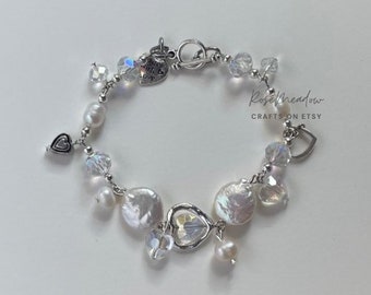 May include: A delicate bracelet featuring a mix of white freshwater pearls, clear crystal beads, and heart-shaped charms. The bracelet is strung on a silver chain and has a toggle clasp. The Rose Meadow Crafts on Etsy logo is visible.