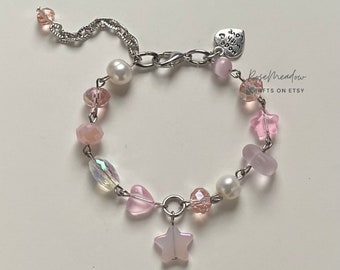 Op de afbeelding: Een roze en zilveren armband met een hartbedel met de tekst "love you always". De armband heeft roze en heldere glazen kralen, parelkraaltjes en een sterbedel.