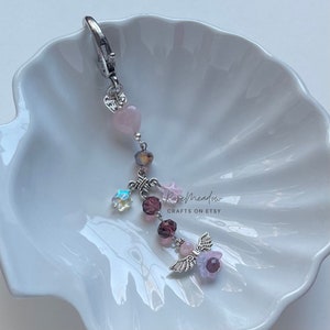 May include: A pink and purple charm with a silver angel wing, heart, and star charms. The charm is attached to a silver key ring. The charm is on a white background. "Rosemeadow Crafts on Etsy" is written on the background.
