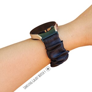 May include: A black silicone watch band with a scrunchie-like design. The band is worn on a silver Samsung Galaxy Watch 4.